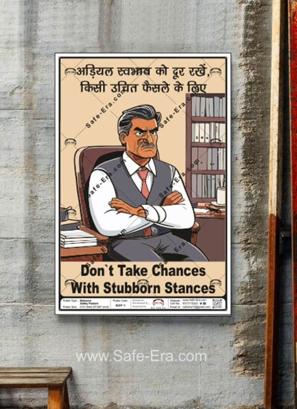 Framed Behaviour Safety Poster 'BSP-1' displayed on a concrete wall. The poster's design features an angry, stubborn-looking man sitting in an office chair with his arms crossed. The text, in English and Hindi, promotes safety by advising: "Don't Take Chances With Stubborn Stances" and "Keep stubborn nature away for an appropriate decision."