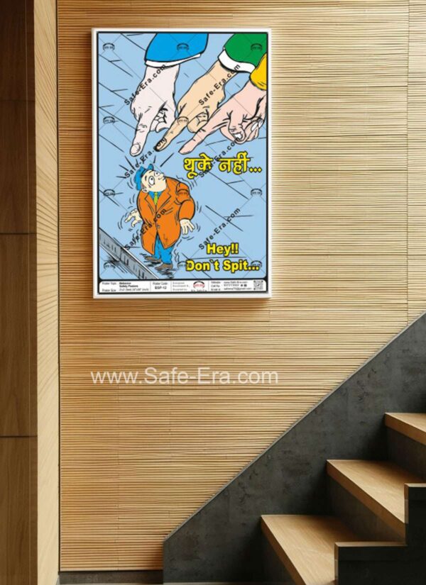 A 'Don't Spit' behaviour safety poster (Code: BSP-12) framed and displayed on a wooden slat wall near a staircase. The poster features a cartoon illustration of a man being pointed at by three giant fingers while standing in a puddle of water/spit. The poster's message clearly states, 'Hey!! Don't Spit...' in English and 'थूके नहीं...' in Hindi, promoting cleanliness and hygiene.