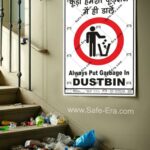 A 'Always Put Garbage In DUSTBIN' behaviour safety poster (Code: BSP-24) displayed next to a stairwell covered in litter. The poster features a universally recognized symbol of a person throwing trash into a bin inside a large red 'prohibited' circle. The message clearly reinforces hygiene and cleanliness in English and Hindi.